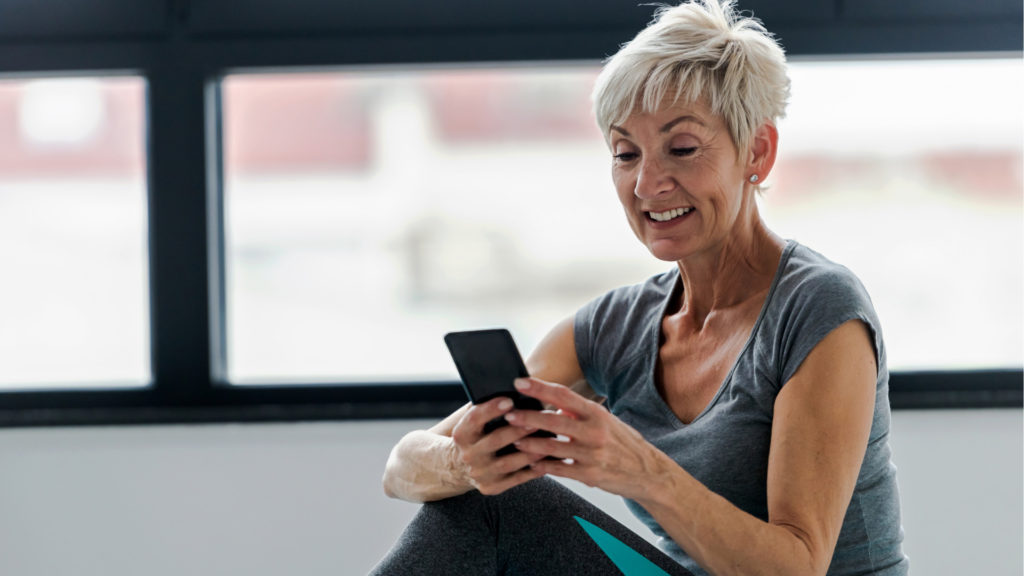 Ältere Dame in Sportkleidung, die das Handy in der Hand hält